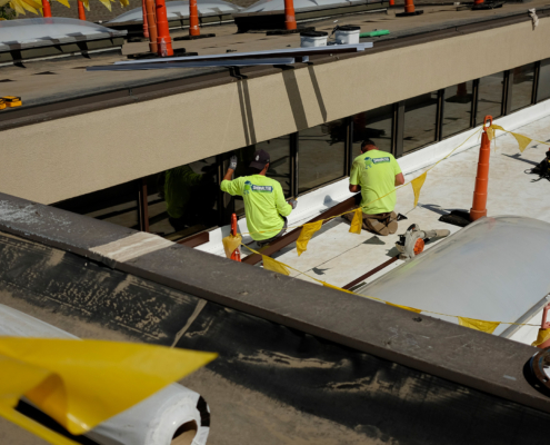 Two Men In Bright Green Shirts With Company Branding Working On Roof